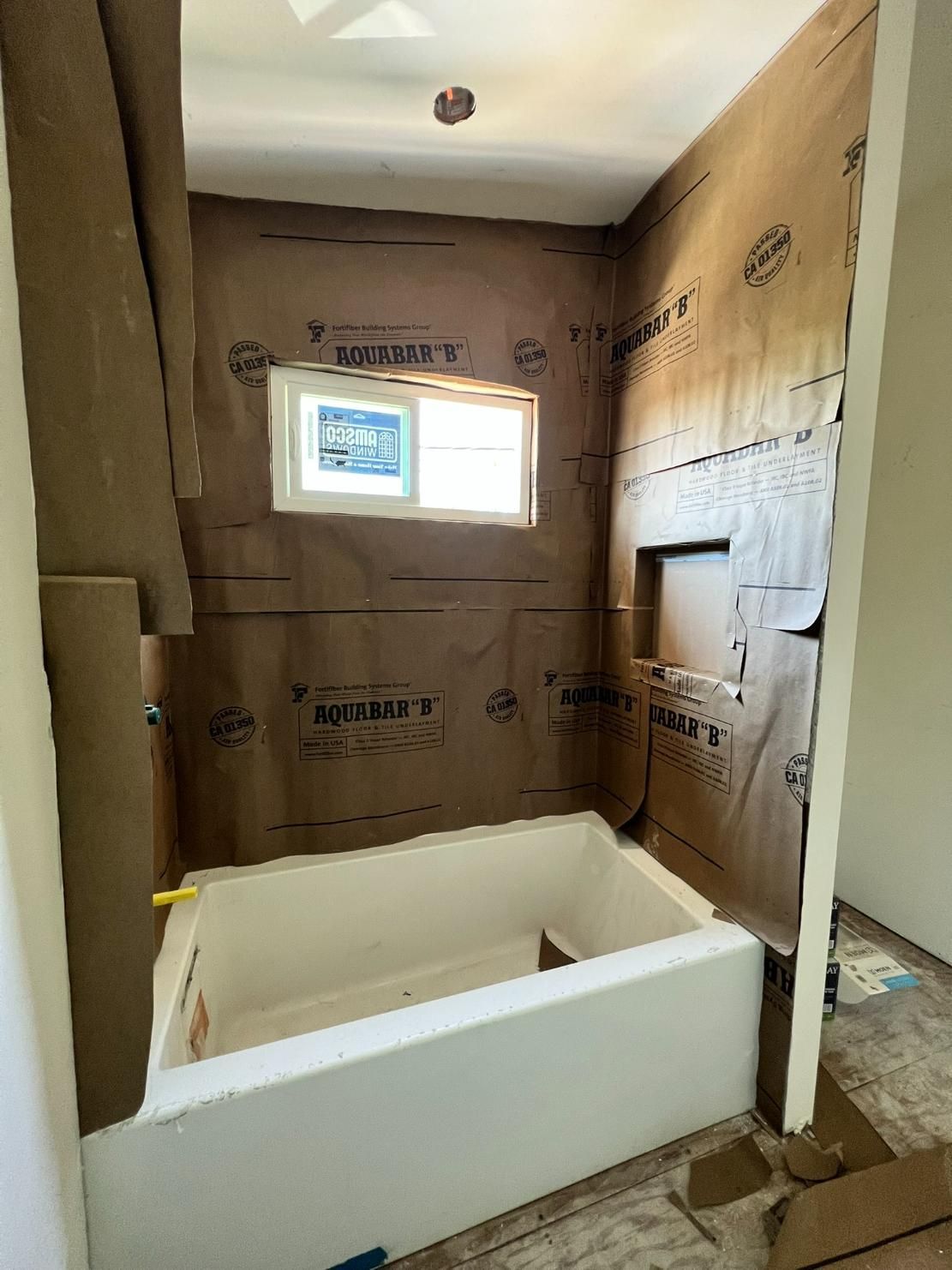 Unfinished bathroom with a white bathtub, window, and insulation exposed on the walls.