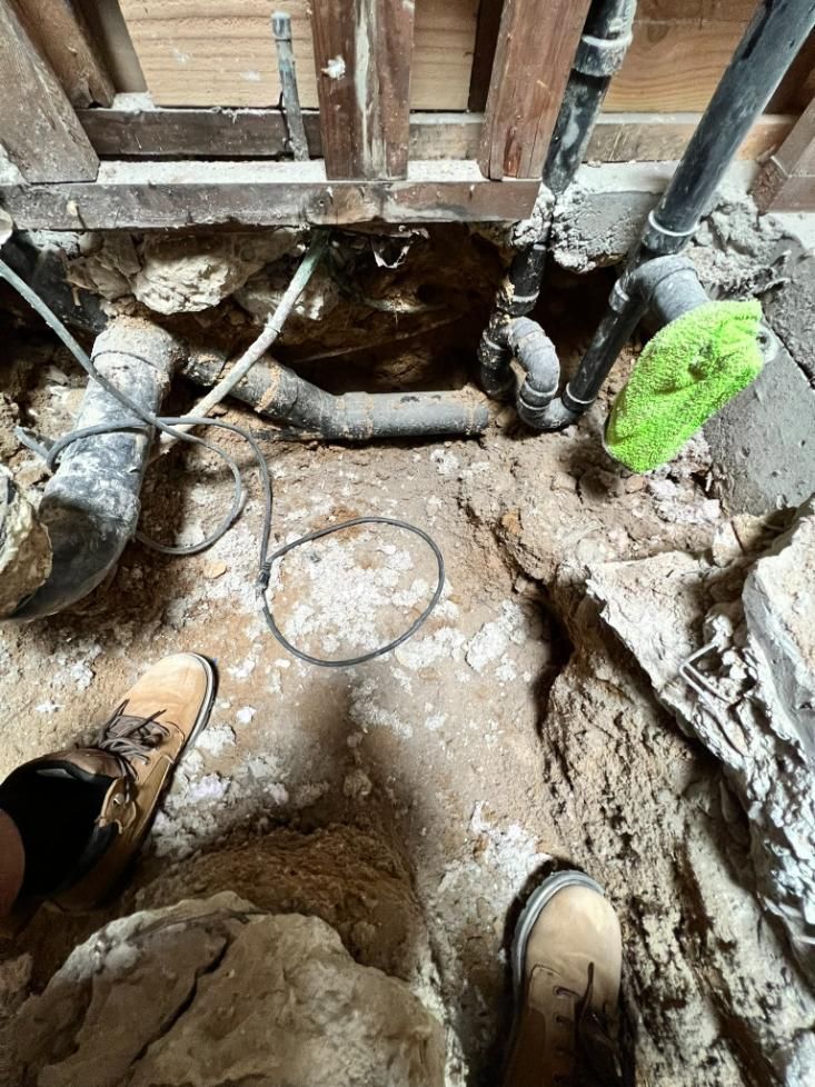 Dirty indoor construction site with exposed floor hole, pipes, boots, and a green cloth on the right