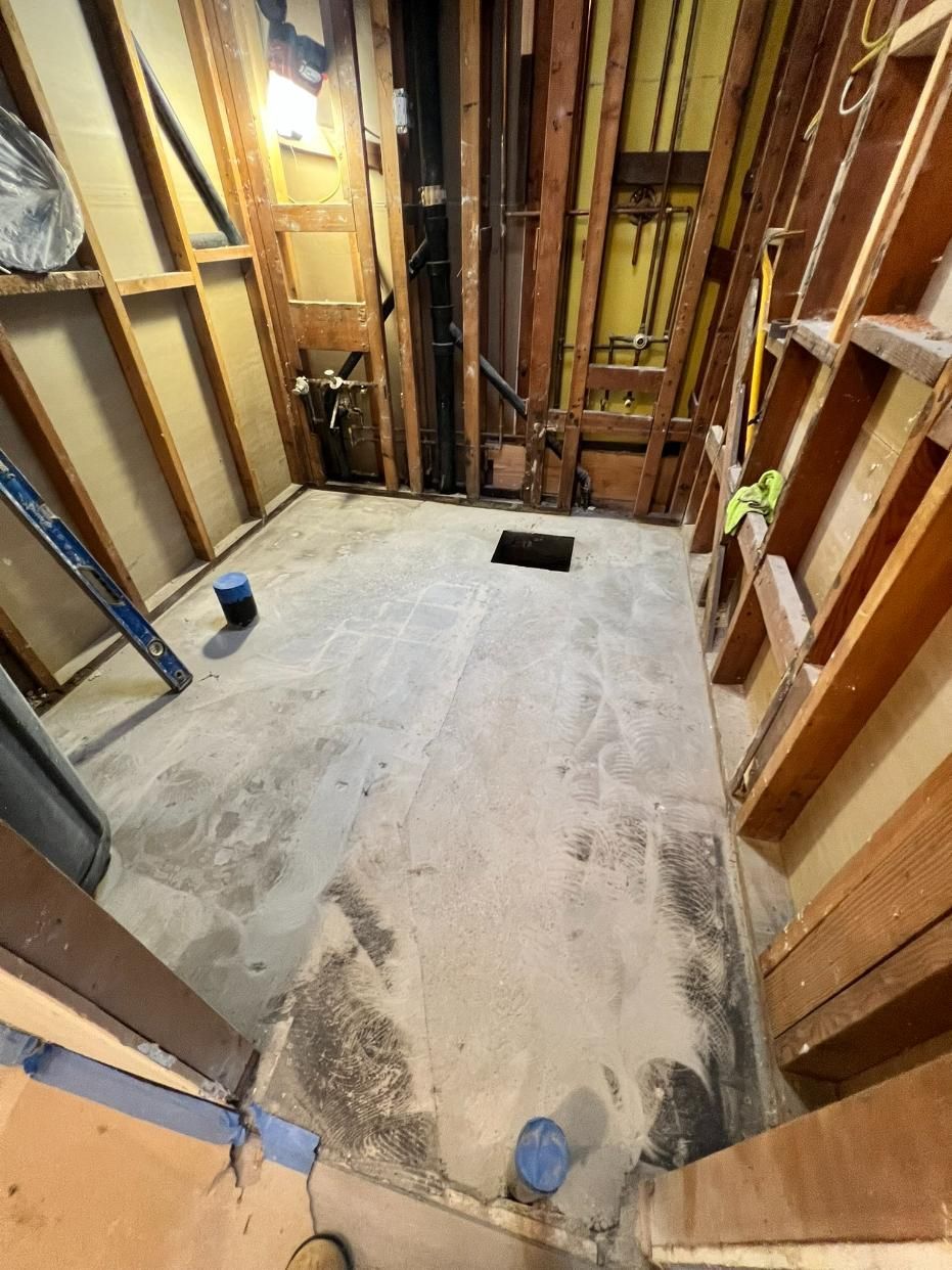 Unfinished basement room with exposed studs, concrete floor, and a small floor opening near the back wall