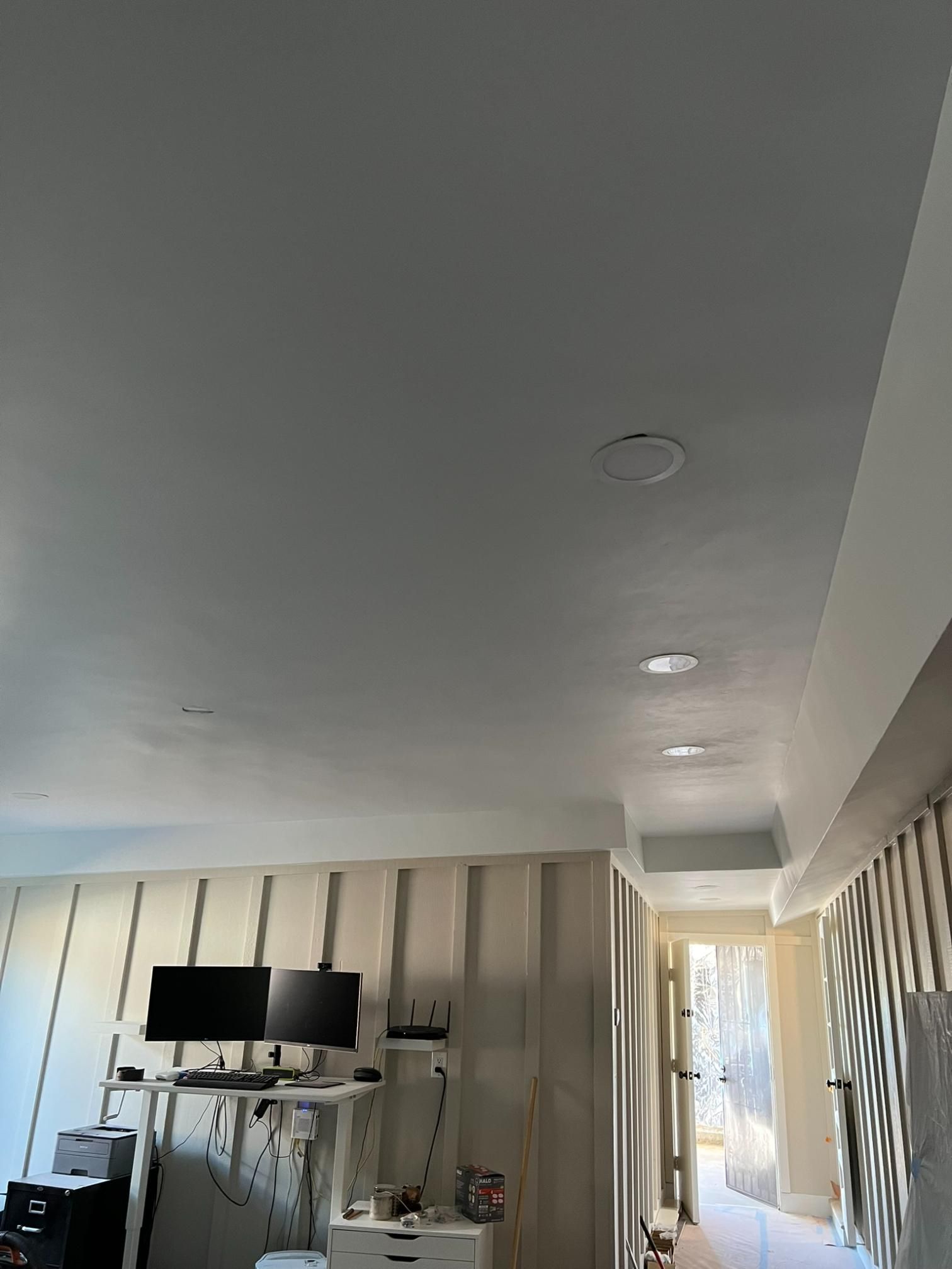 Modern living room with vaulted white ceiling, TV on a console, and bright hallway beyond.