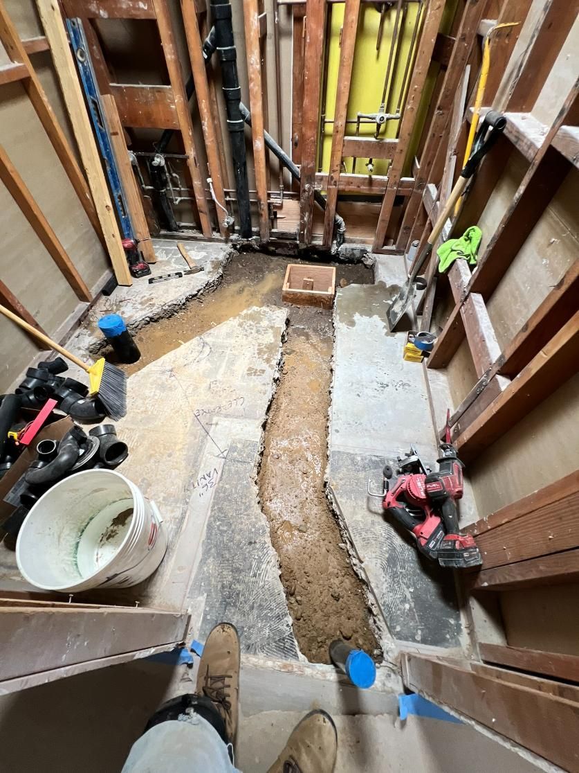 Narrow hallway under renovation with exposed studs, tools, buckets, and a dirt trench through the floor.