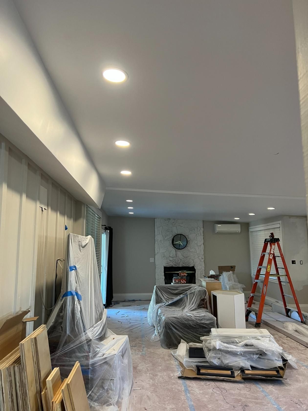 Renovation room with covered furniture, ladder, tools, and recessed ceiling lights.
