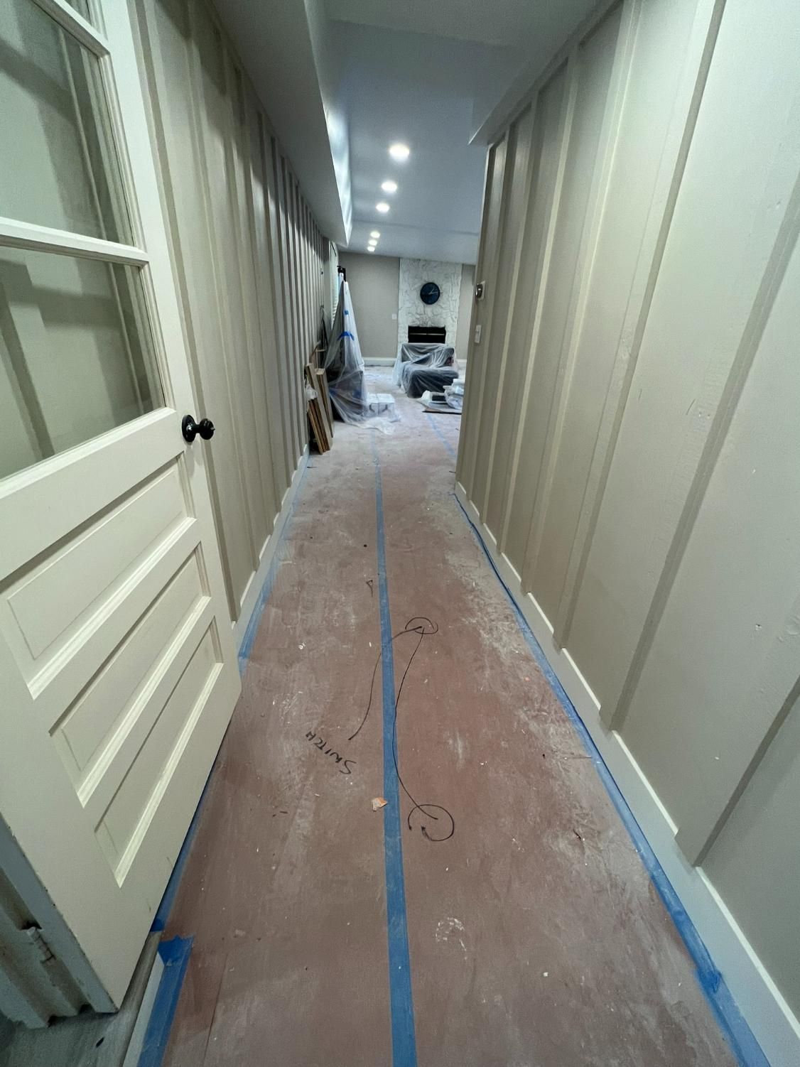 Narrow hallway under renovation with taped floor, exposed drywall, and lights overhead