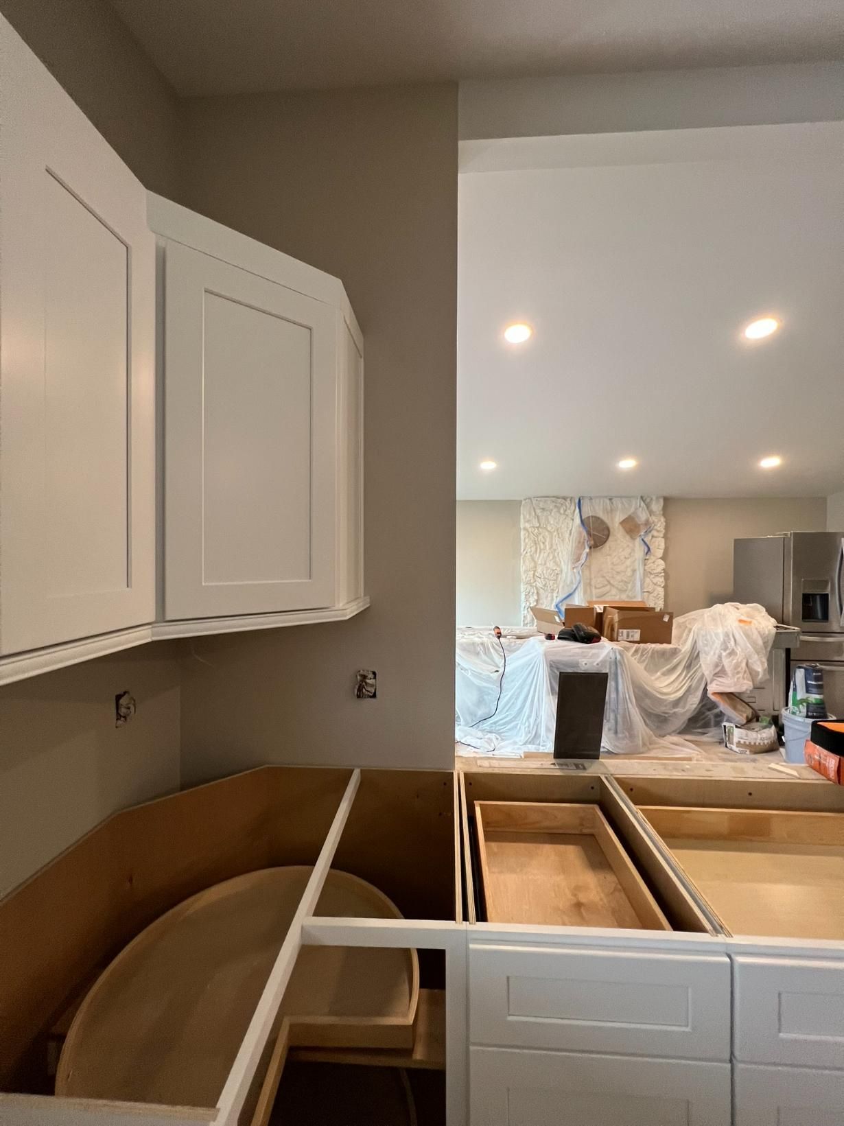 Kitchen renovation in progress with white cabinets, countertop frames, and tools in a bright room