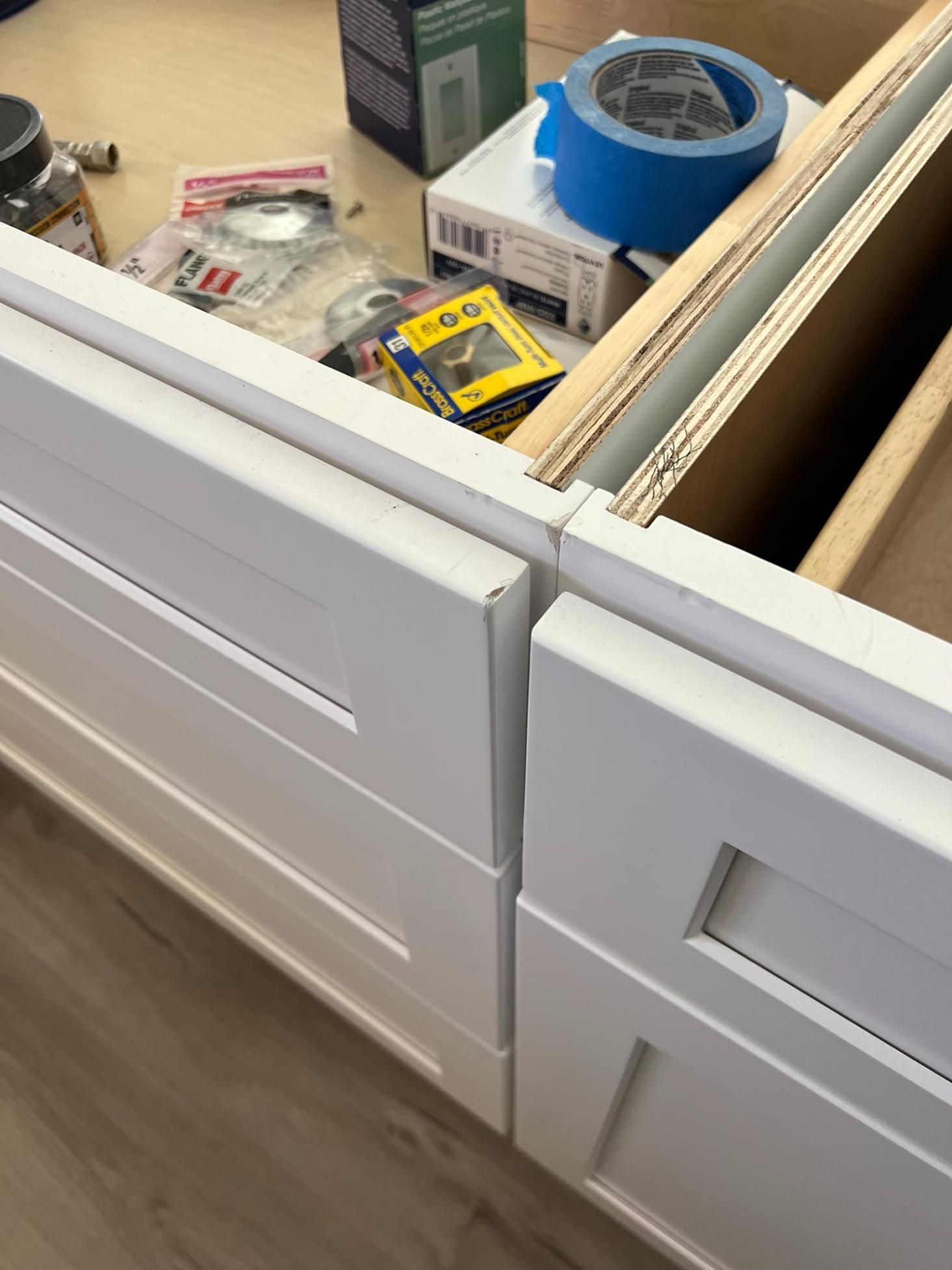 Open drawer with tools, tape, and supplies in a white kitchen cabinet.
