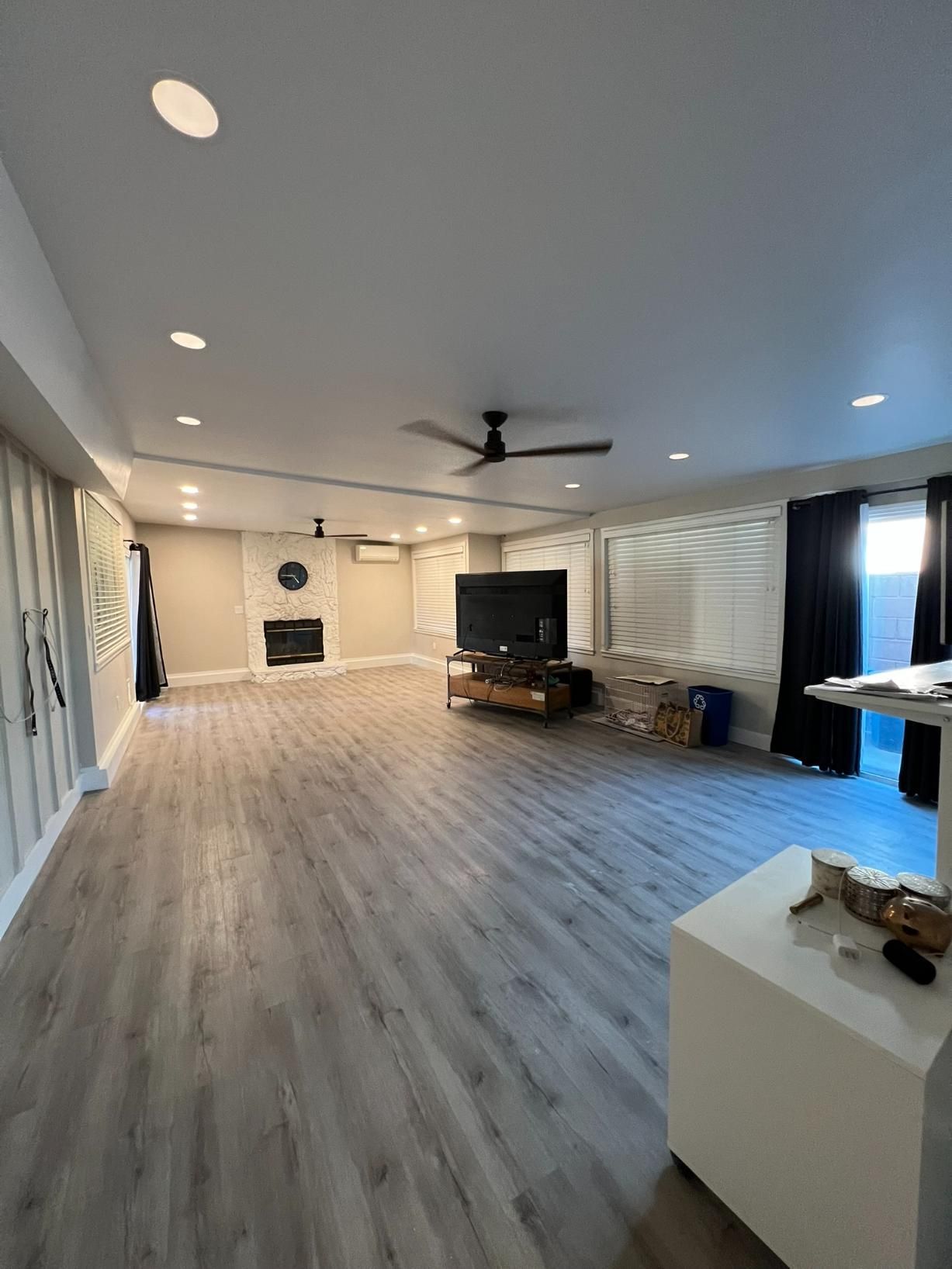 Spacious living room with gray floors, white walls, ceiling fans, TV, fireplace, and blue curtains