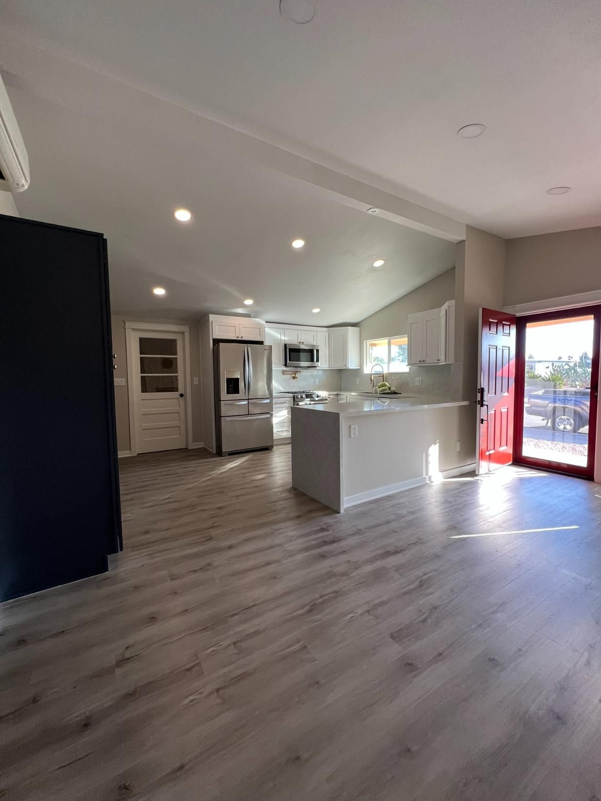 Bright open kitchen and living area with light wood floors, white cabinets, and red glass doors to outside.