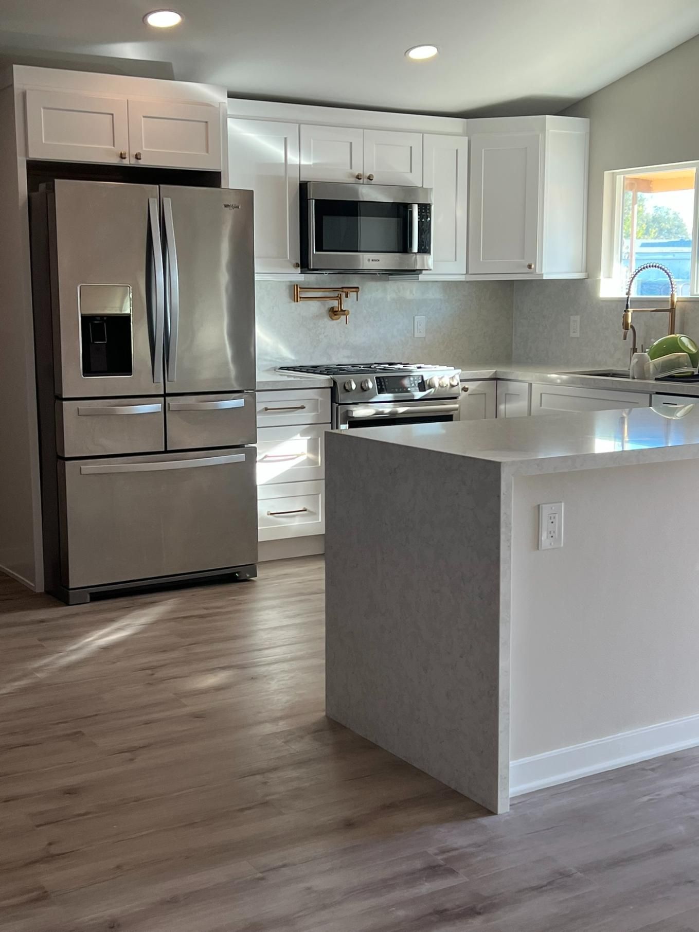 Modern white kitchen with stainless steel appliances, island, and wood-look flooring