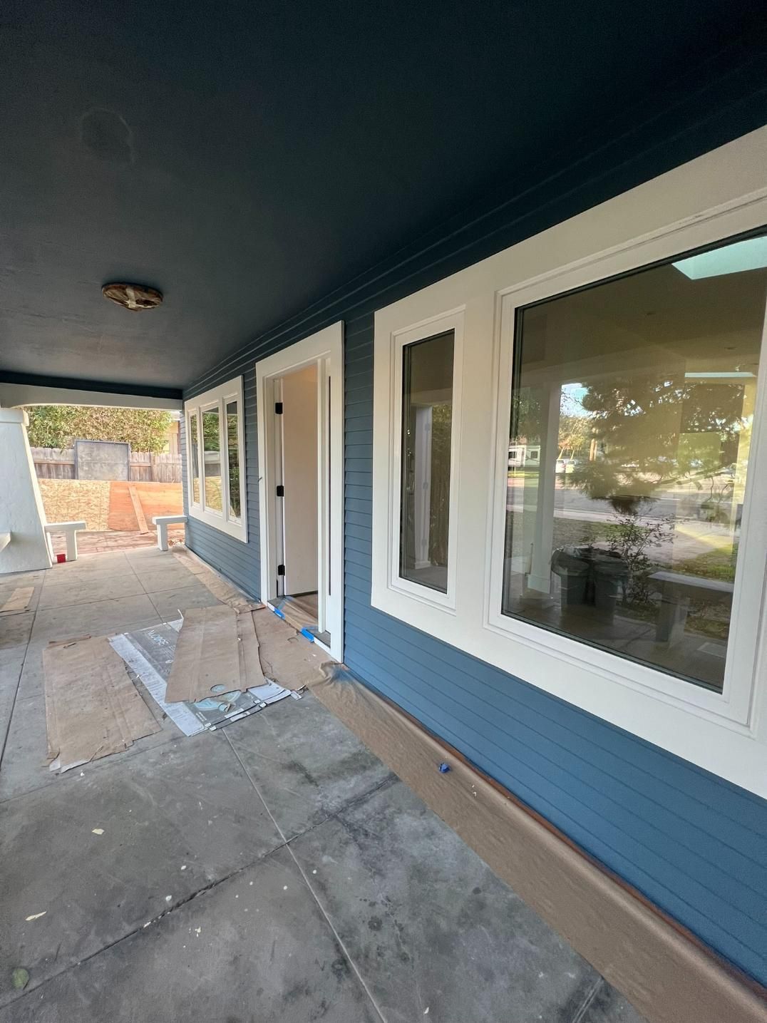 Covered porch with blue siding, white-trimmed windows, and a concrete floor under construction
