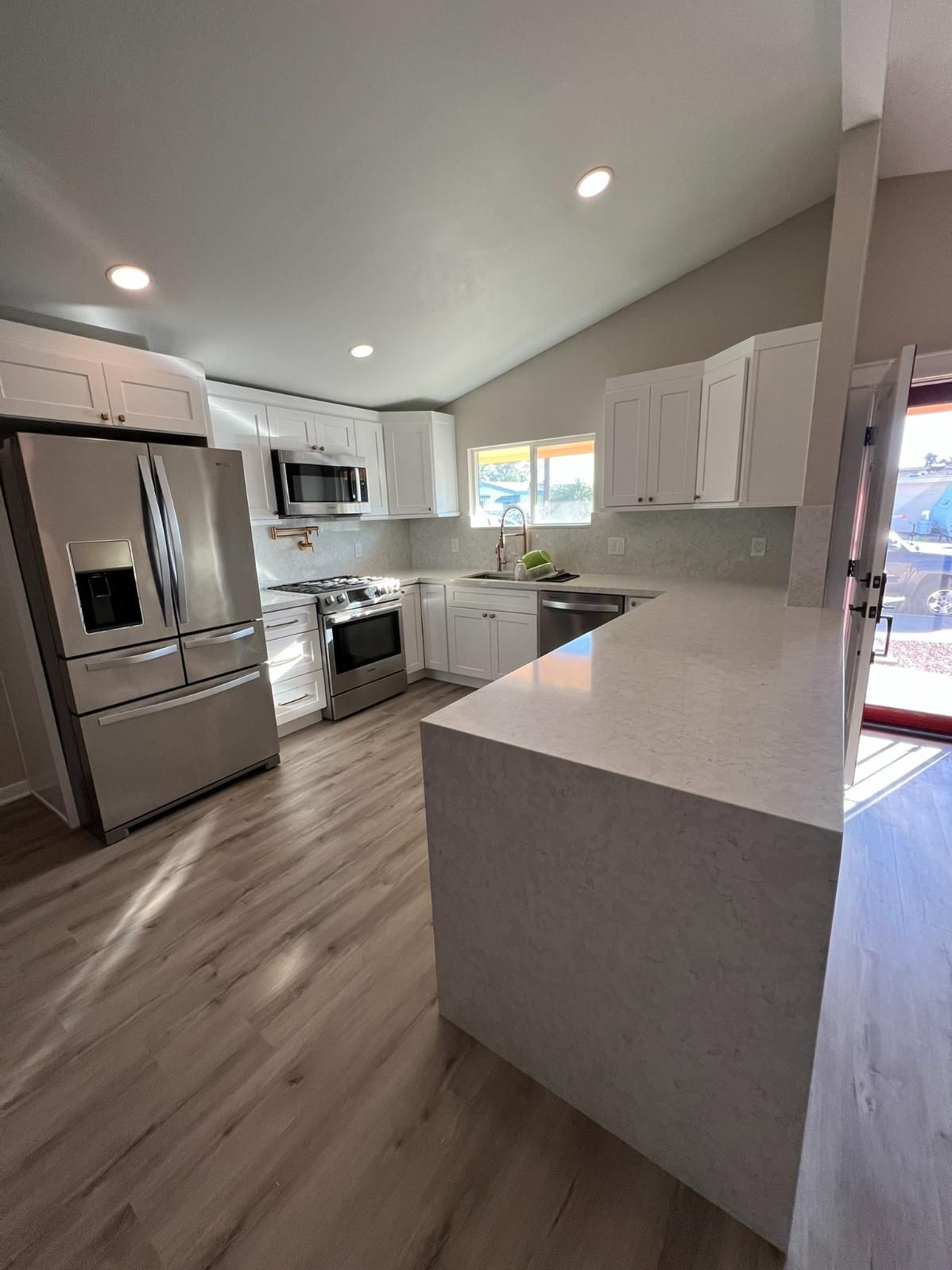 Bright modern kitchen with stainless appliances, white cabinets, and a large island under recessed lights
