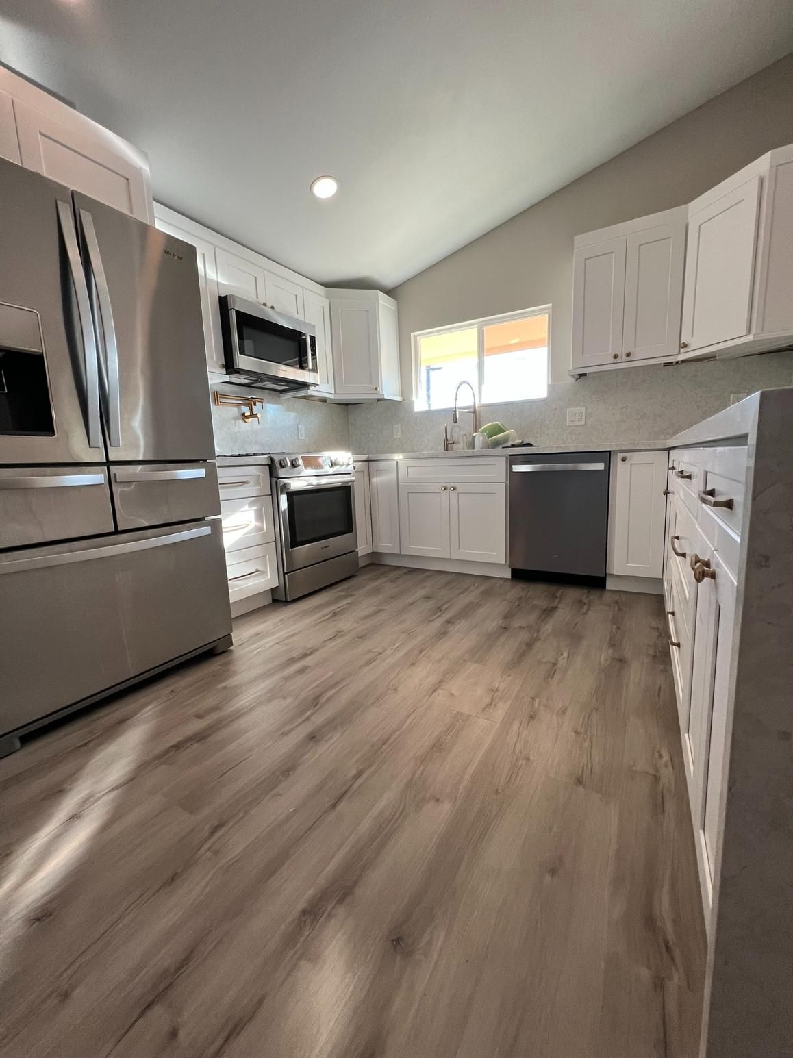 Bright modern kitchen with stainless steel appliances, white cabinets, and wood-look flooring