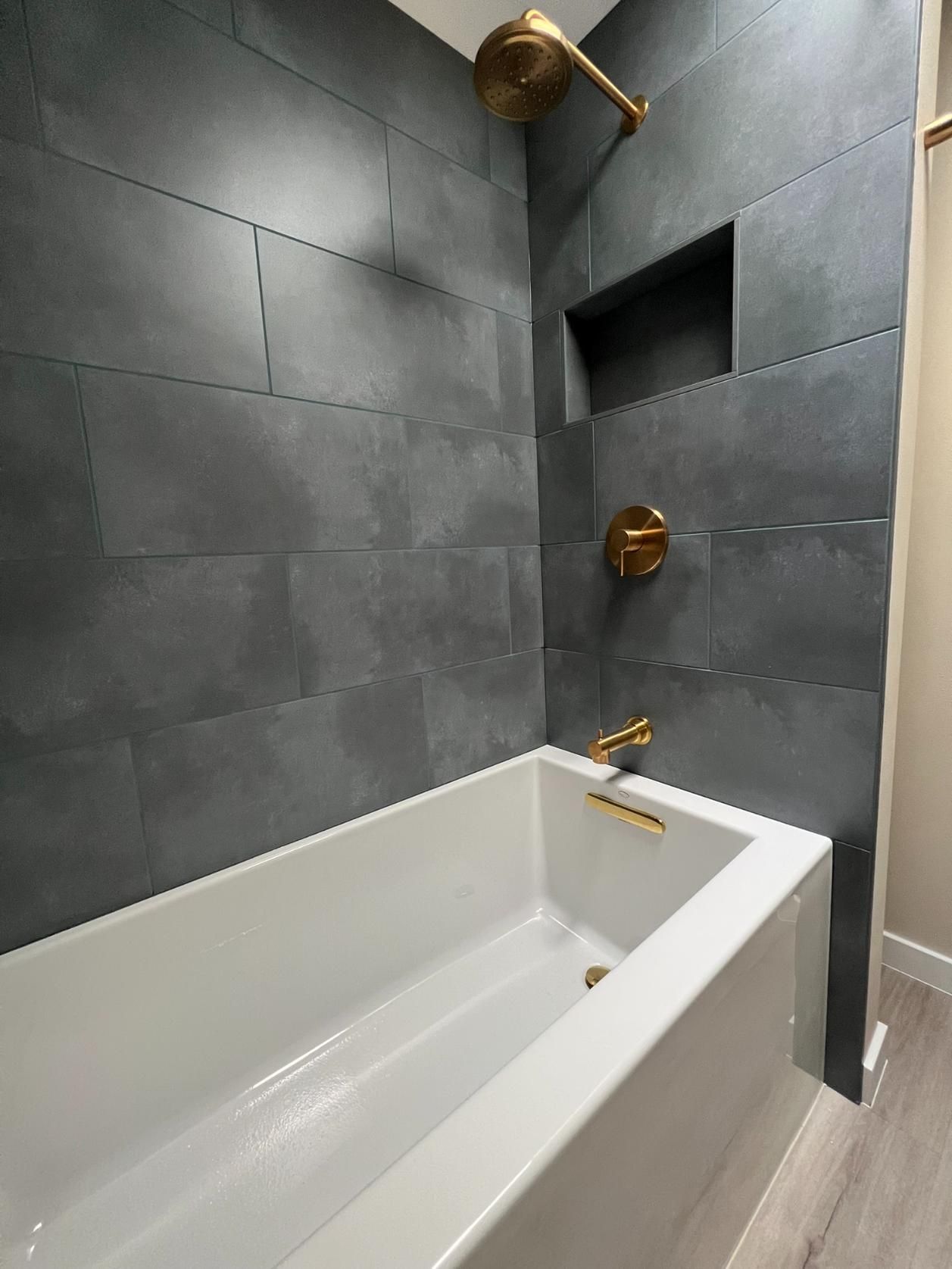 Modern bathroom with white bathtub, dark gray tile walls, and brass shower fixtures