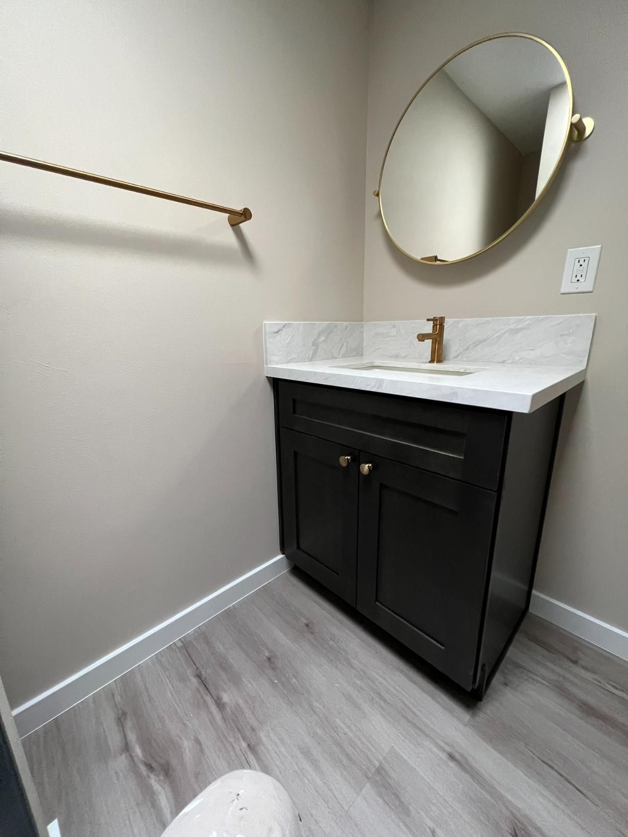 Small bathroom vanity with black cabinet, marble sink, round mirror, and towel bar on beige walls.