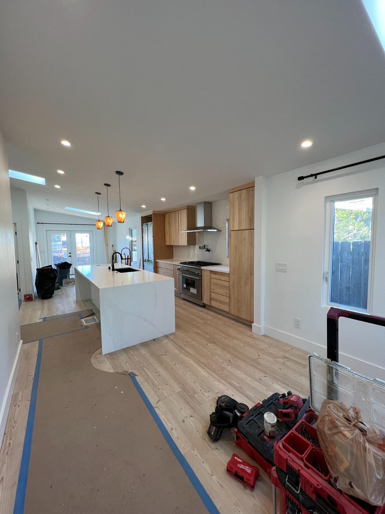 Renovated kitchen with white island and wood cabinets, under construction with tools and taped floor area