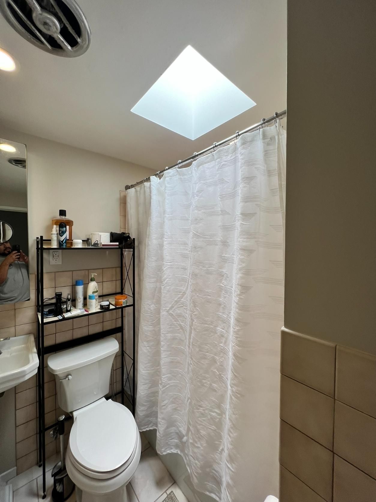Small bathroom with toilet, shelving unit, shower curtain, and skylight.