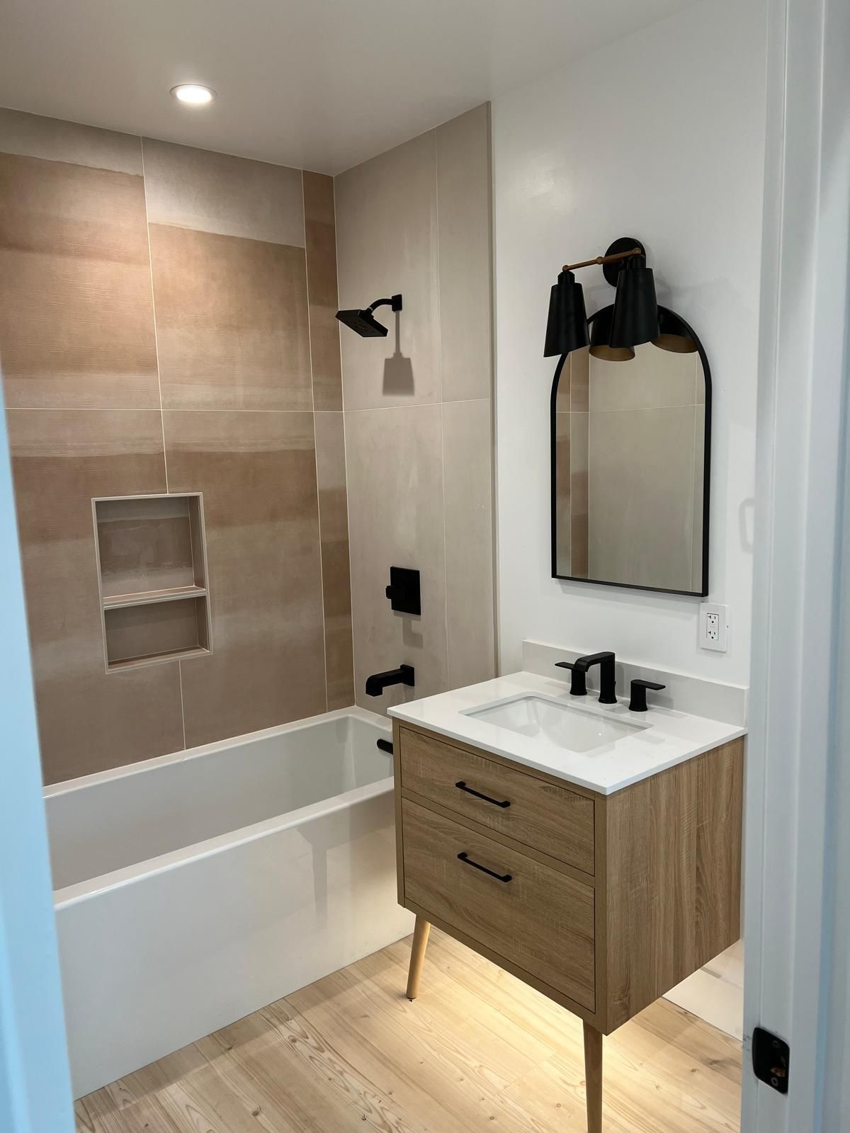 Modern bathroom with tiled tub-shower, wood vanity, black fixtures, and wall mirror