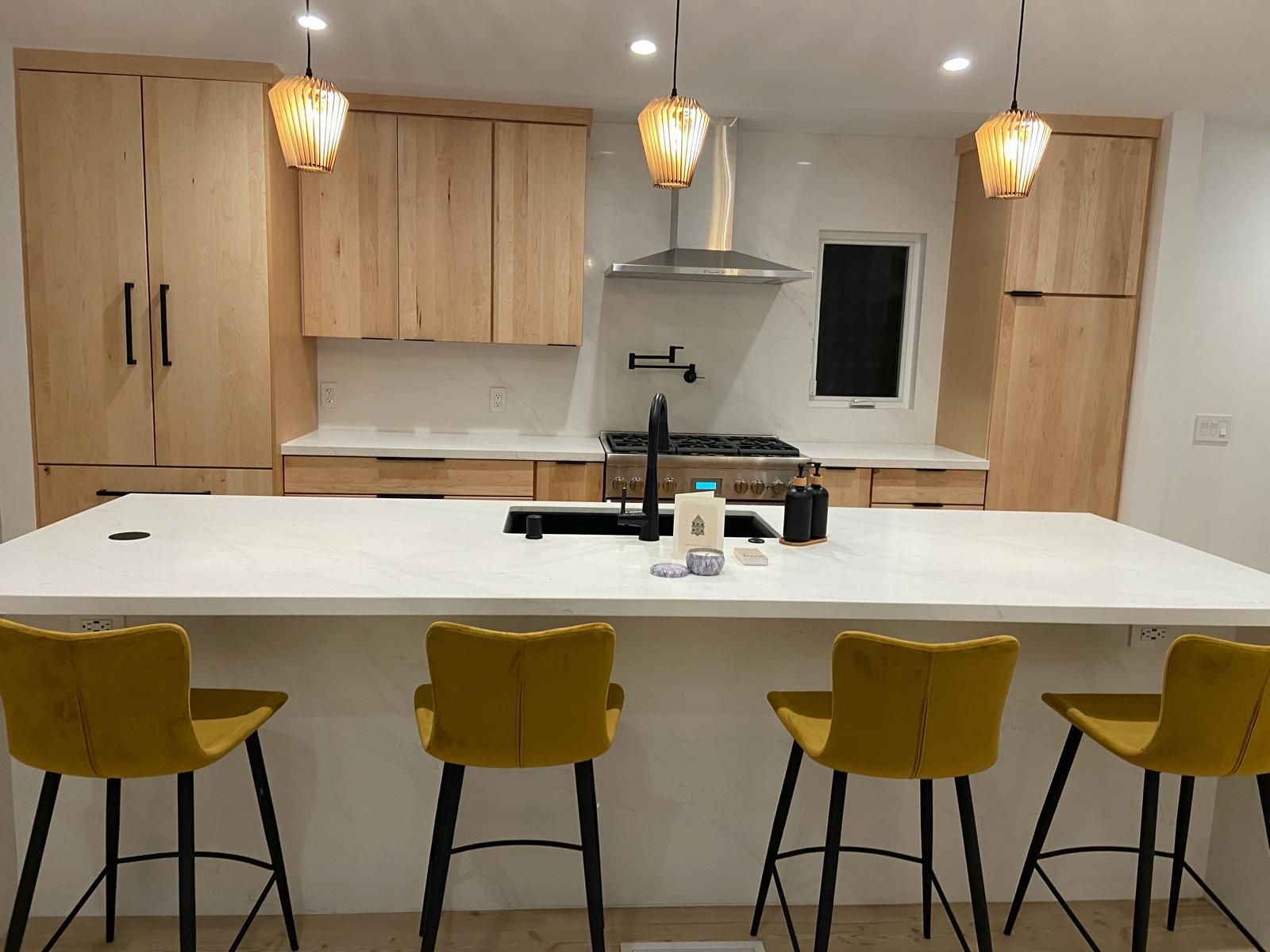 Modern kitchen with white island, yellow stools, wood cabinets, and pendant lights