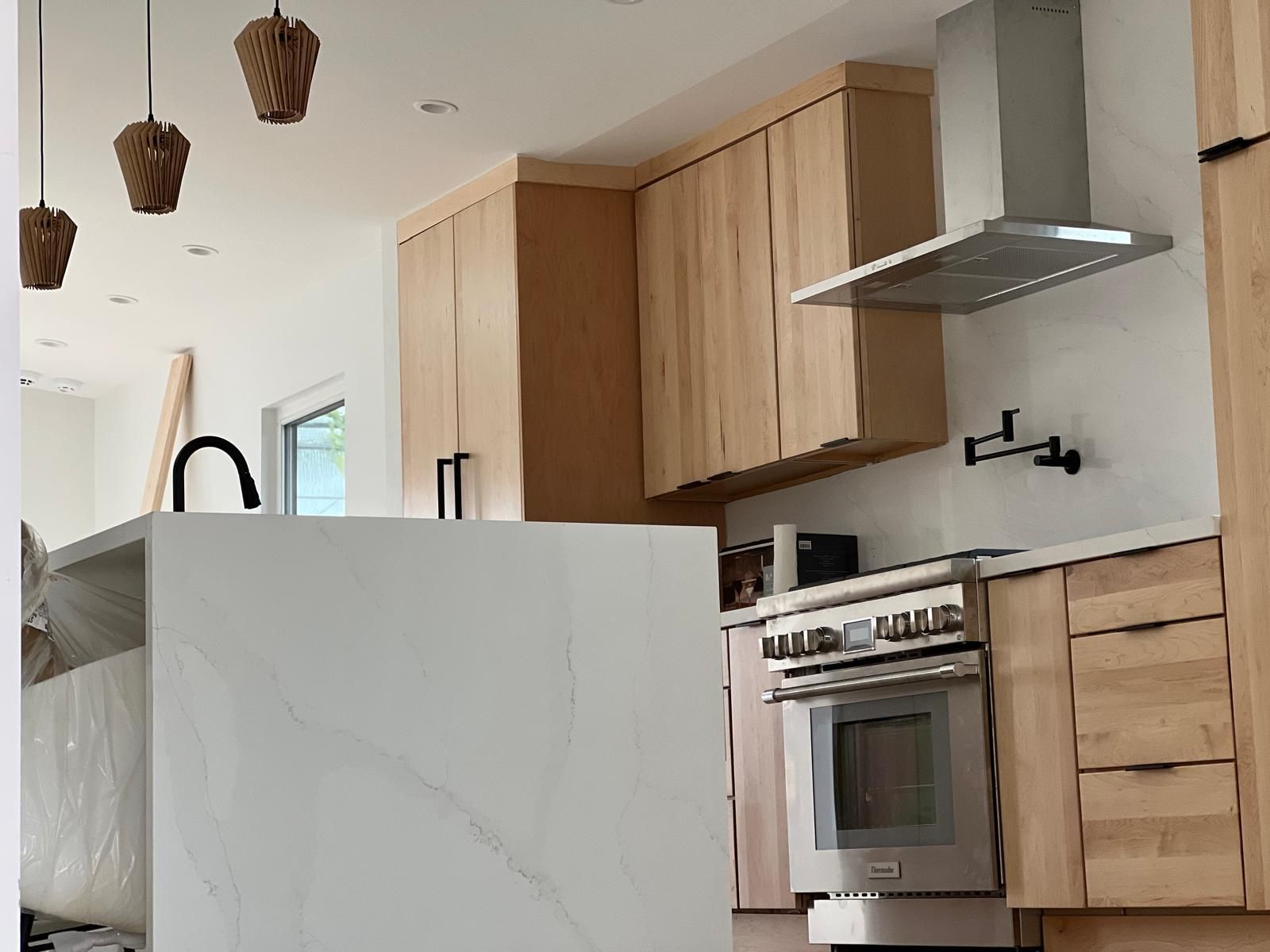 Modern kitchen with light wood cabinets, stainless steel oven, white island, and hanging woven light fixtures