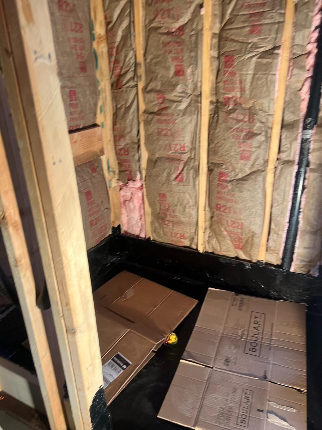 Insulated wall cavity under construction with cardboard floor covering and wood framing.