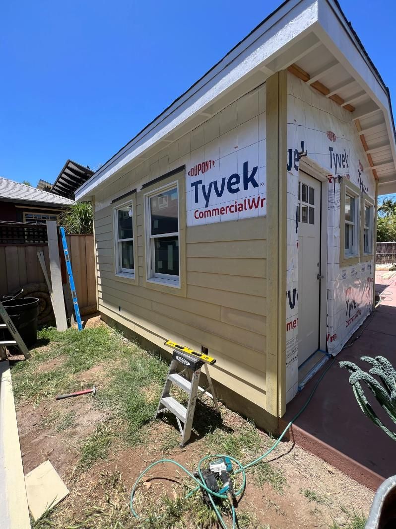 Partially built house exterior with Tyvek house wrap and window openings under bright sunlight