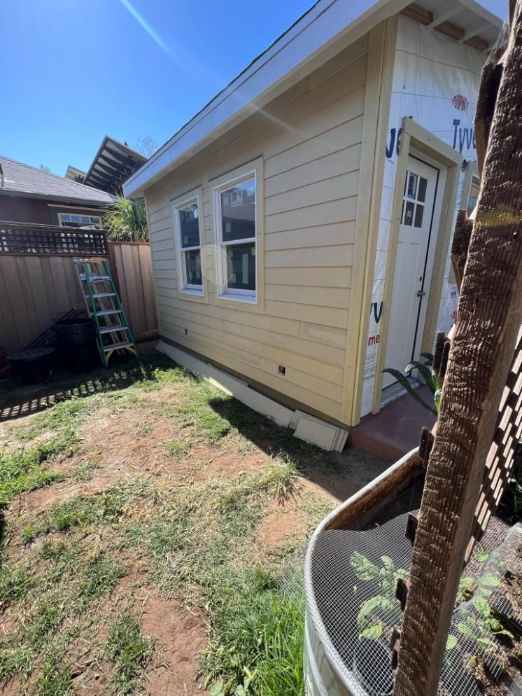 Beige house exterior with windows and a small grassy yard beside a fence and ladder