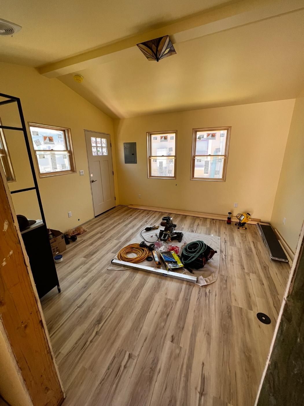 Empty unfurnished room with wood-look floors, cream walls, and scattered items on the floor.