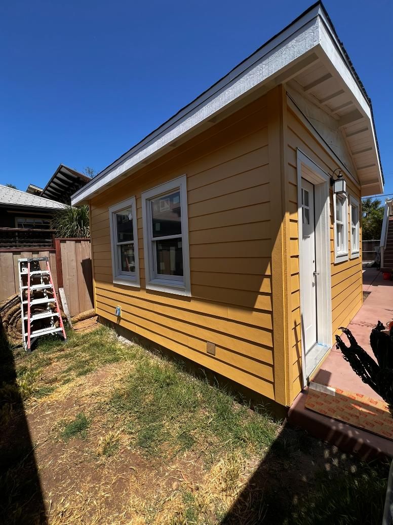 Yellow house exterior with white-trimmed windows, small lawn, and wooden steps under a bright sky
