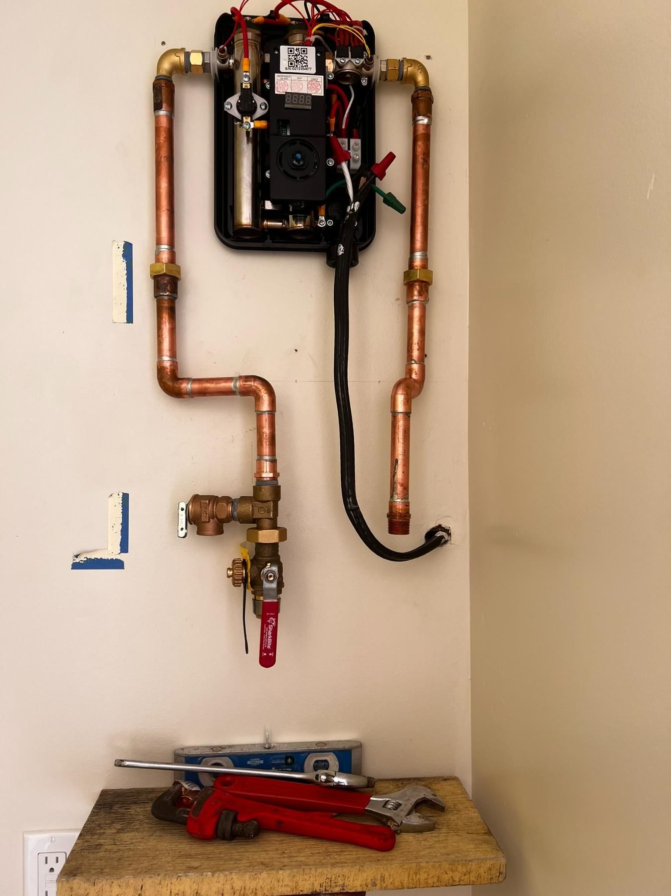 Copper pipes and a wall-mounted water heater in a utility closet, with tools on the floor.