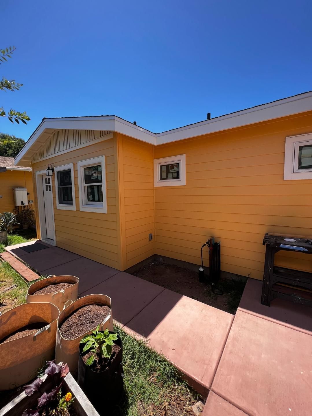 Yellow house exterior with white trim, red walkway, and potted plants under a blue sky