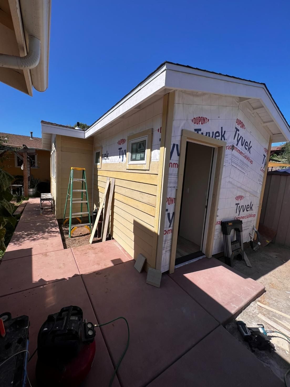 Small yellow house exterior with ladder and tools on a sunny patio