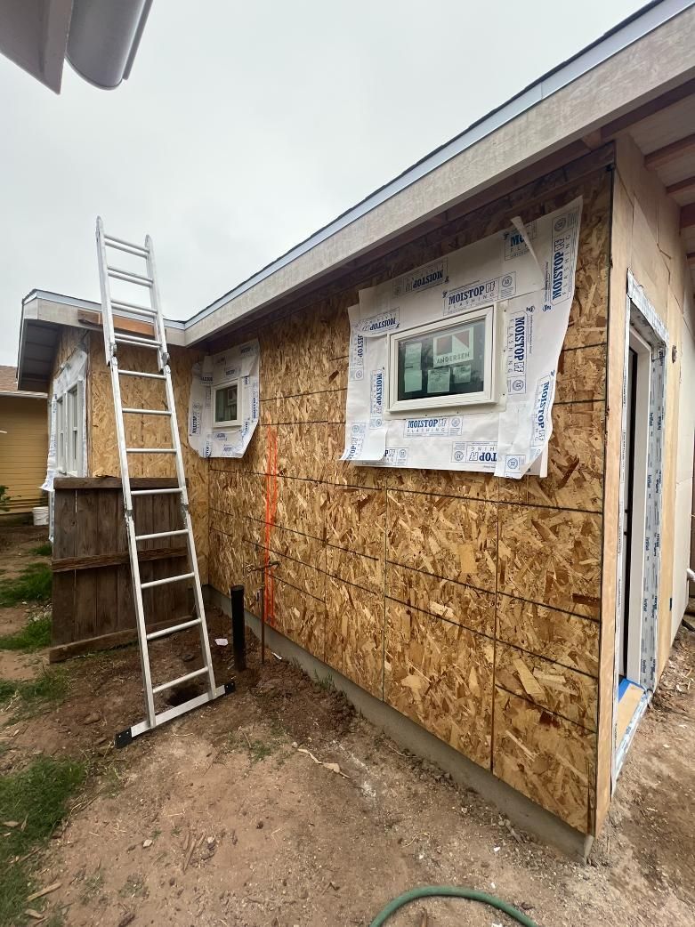 Renovation in progress on a house exterior with OSB sheathing, house wrap, and a ladder leaning against the wall