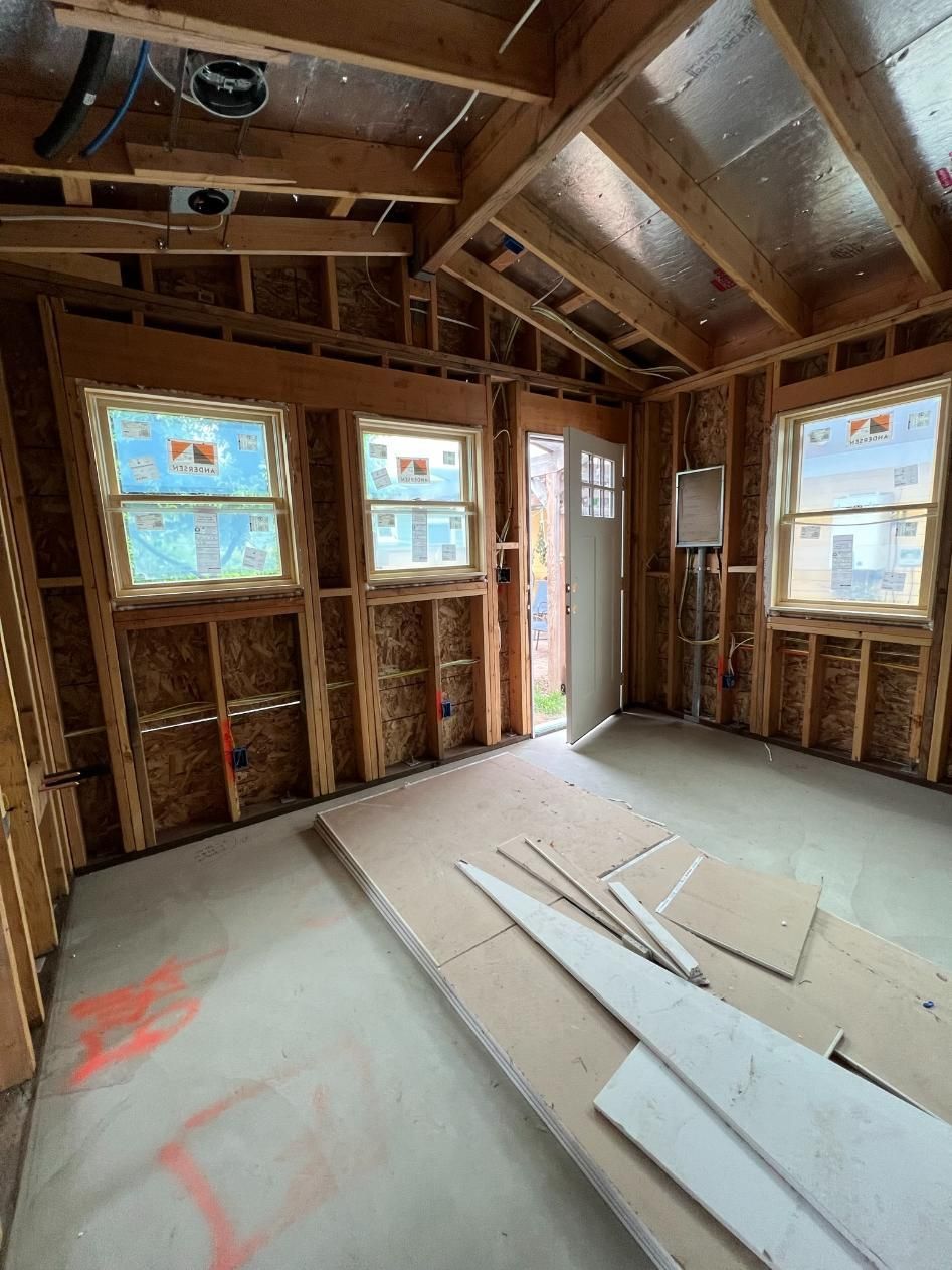 Unfinished room with exposed framing, two windows, open doorway, and construction materials on the floor