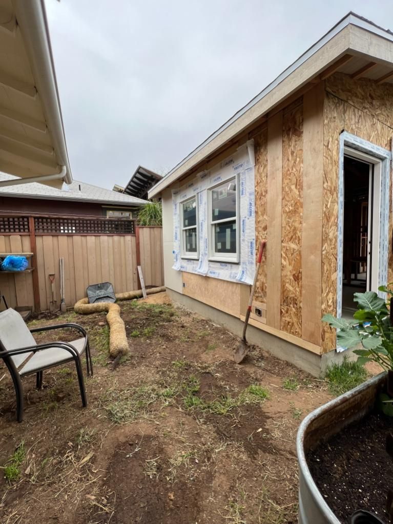 Backyard with a small unfinished house addition, dirt ground, patio chairs, and a wooden fence.