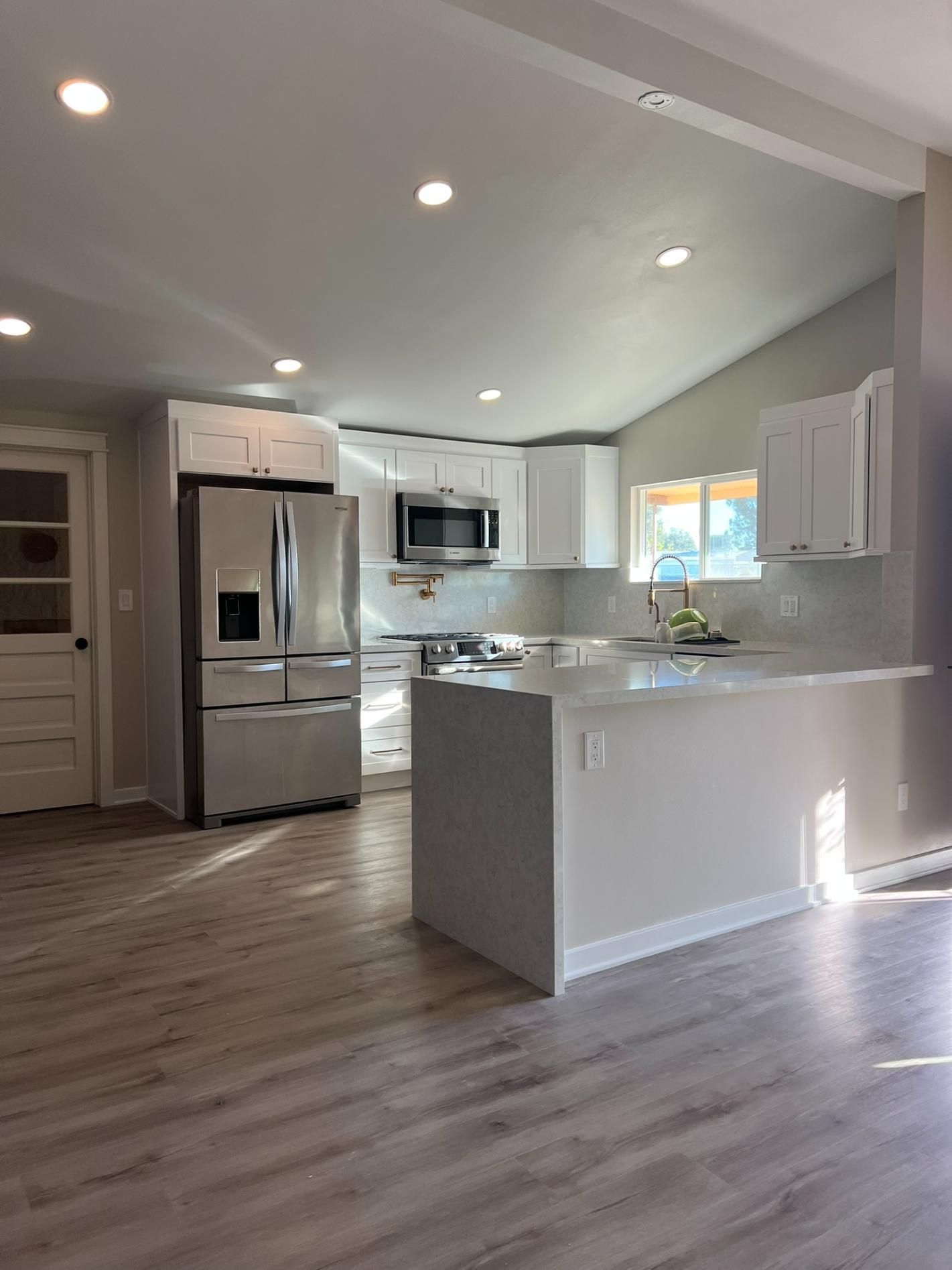 Bright modern kitchen with stainless steel appliances, white cabinets, and a gray island with wood flooring.
