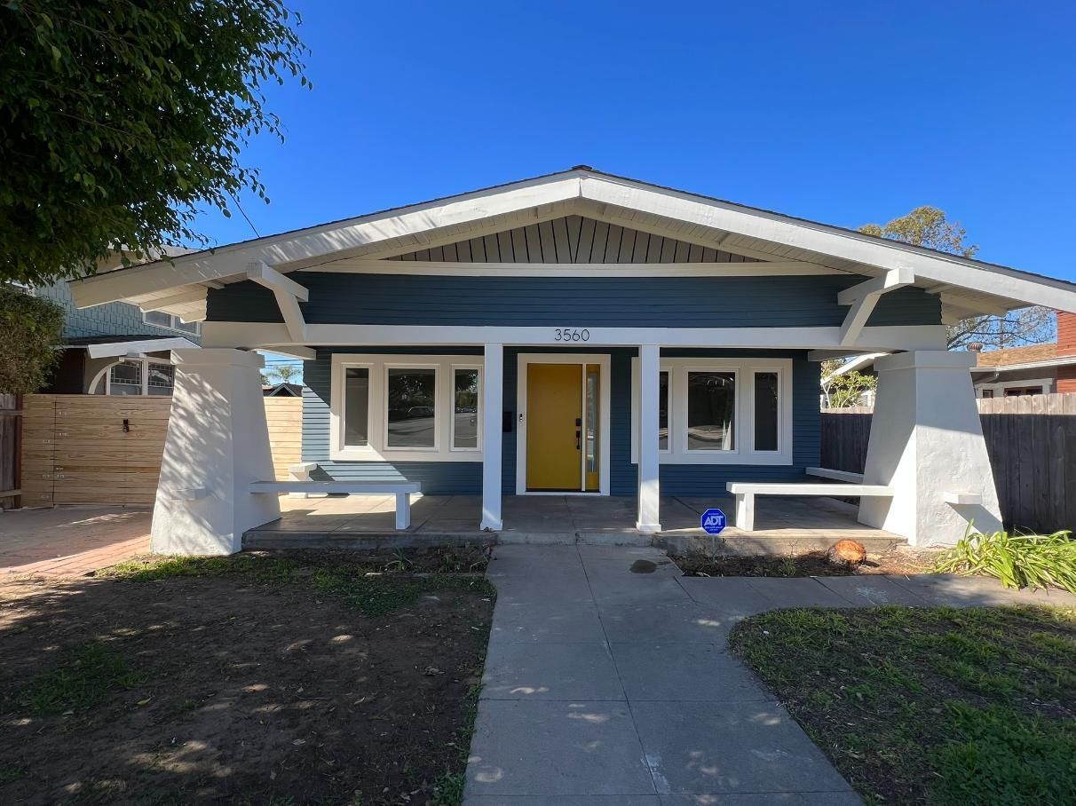 Front view of a blue-gray house with a yellow door and concrete walkway.