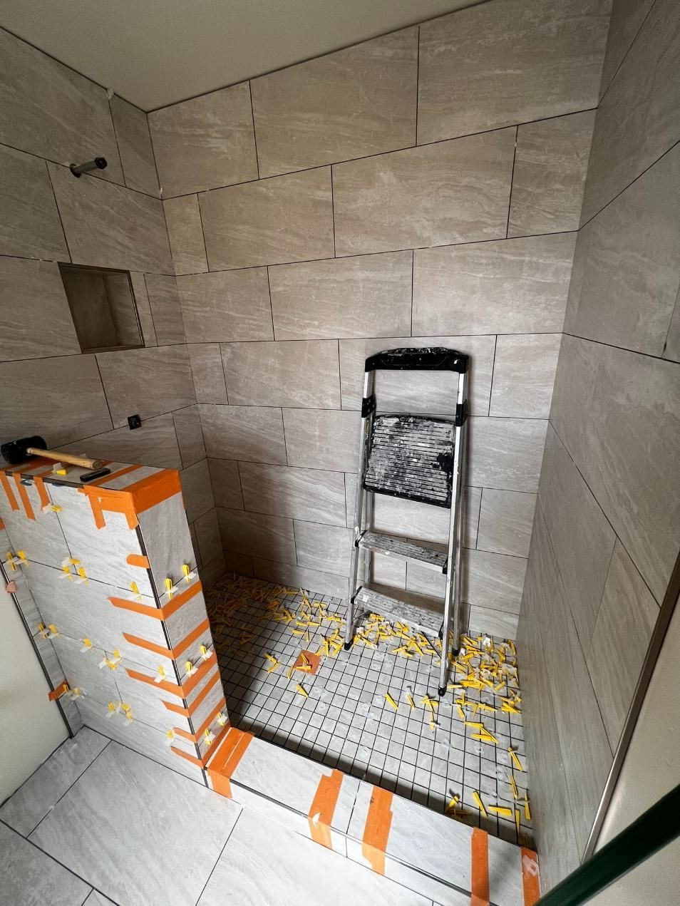 Unfinished tiled shower with a step stool and orange masking tape around the floor and walls.