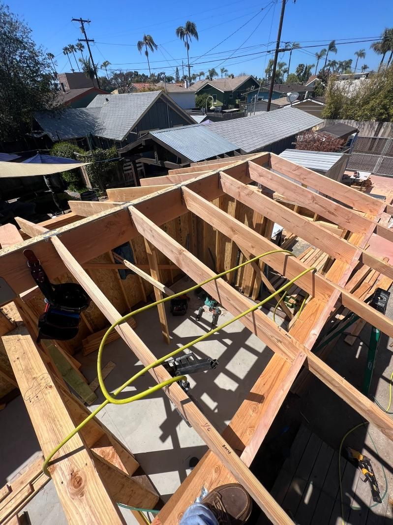 Partially built wooden roof frame on a house under construction, with blue sky and palm trees in the background