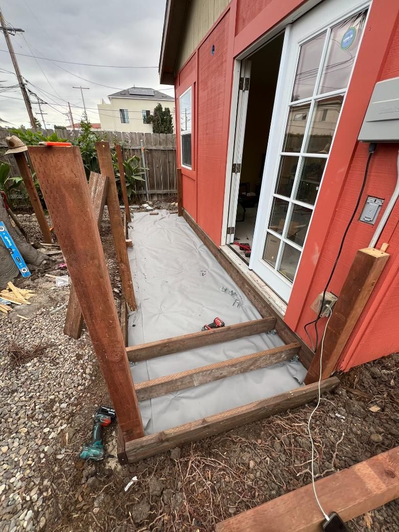 Small concrete porch ramp beside a red house, with wooden posts and steps leading to a glass door.