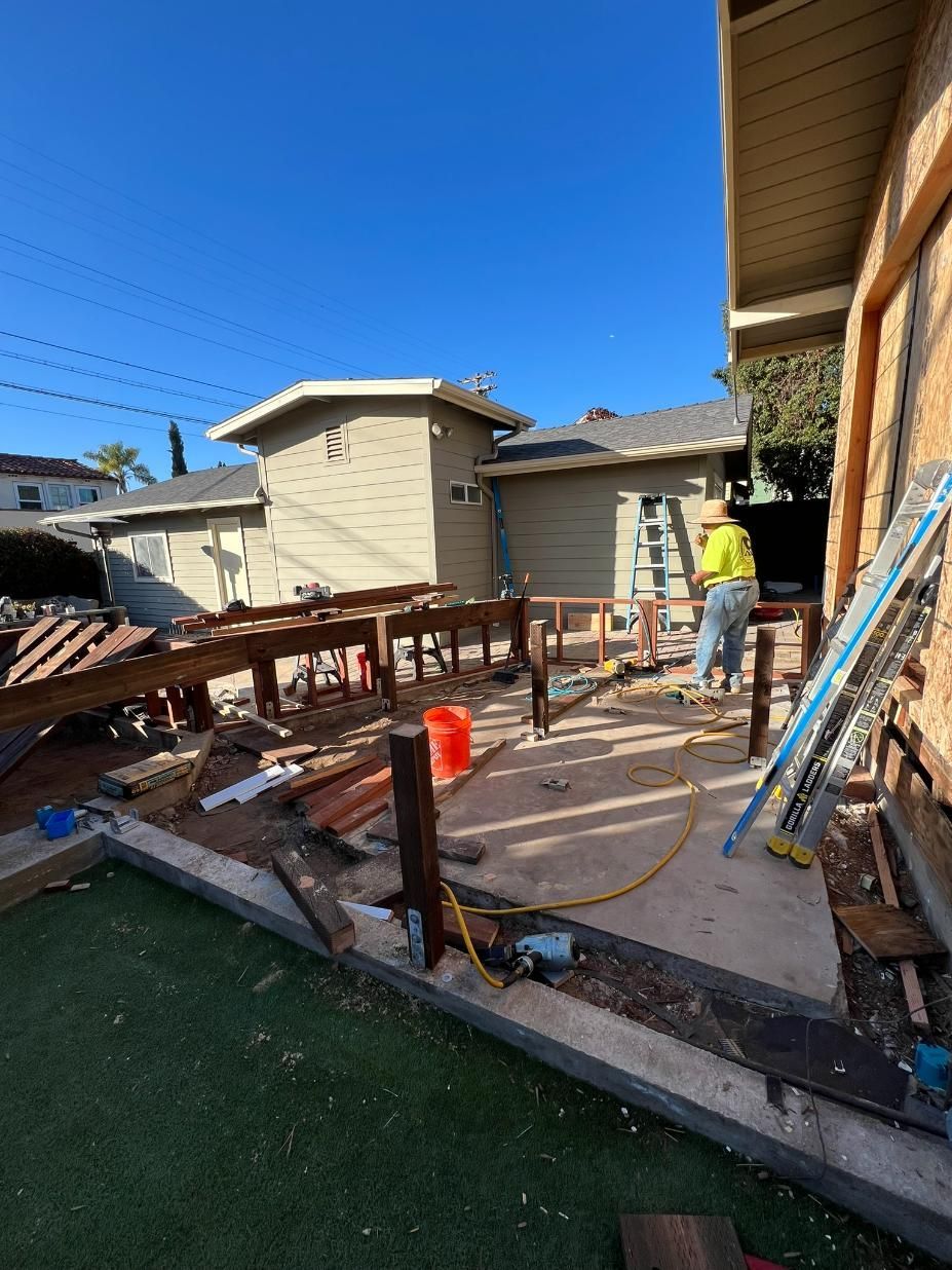Backyard deck under construction with worker, wood framing, tools, and blue sky