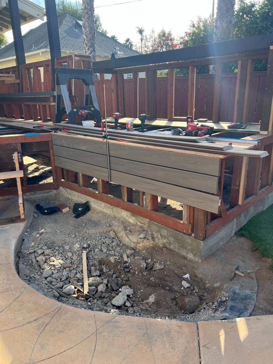 Backyard deck under construction with exposed framing and a gravel work area below