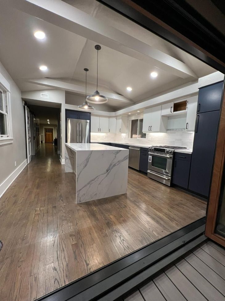 Modern kitchen with marble island, white cabinets, dark wood floors, and pendant lights