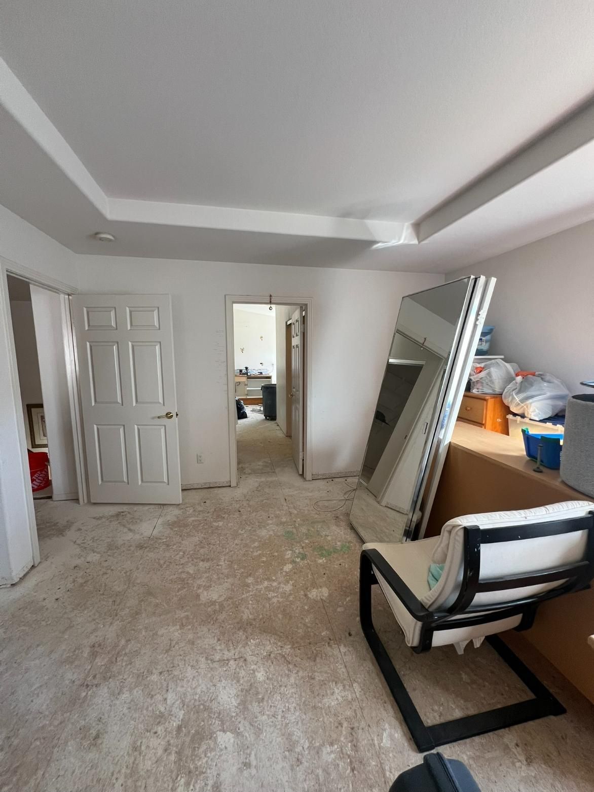 Empty bedroom under renovation with carpet, open closet, leaning mirrors, and storage items by the window.