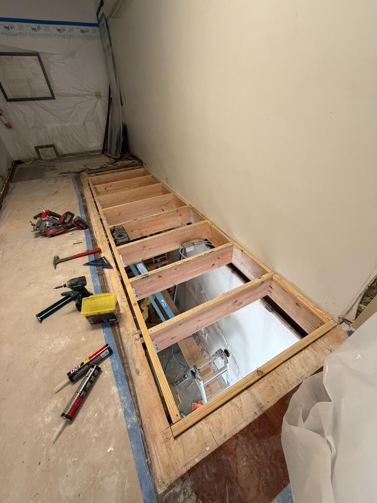 Partially rebuilt floor with exposed joists and tools in a narrow room