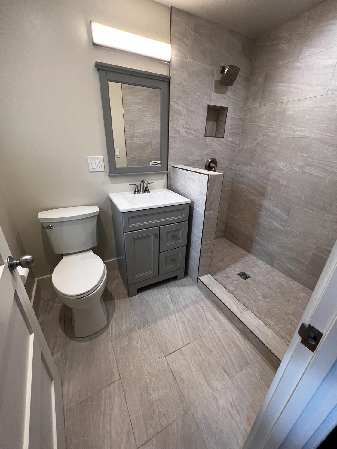 Small bathroom with toilet, vanity sink, mirror, and tiled walk-in shower.