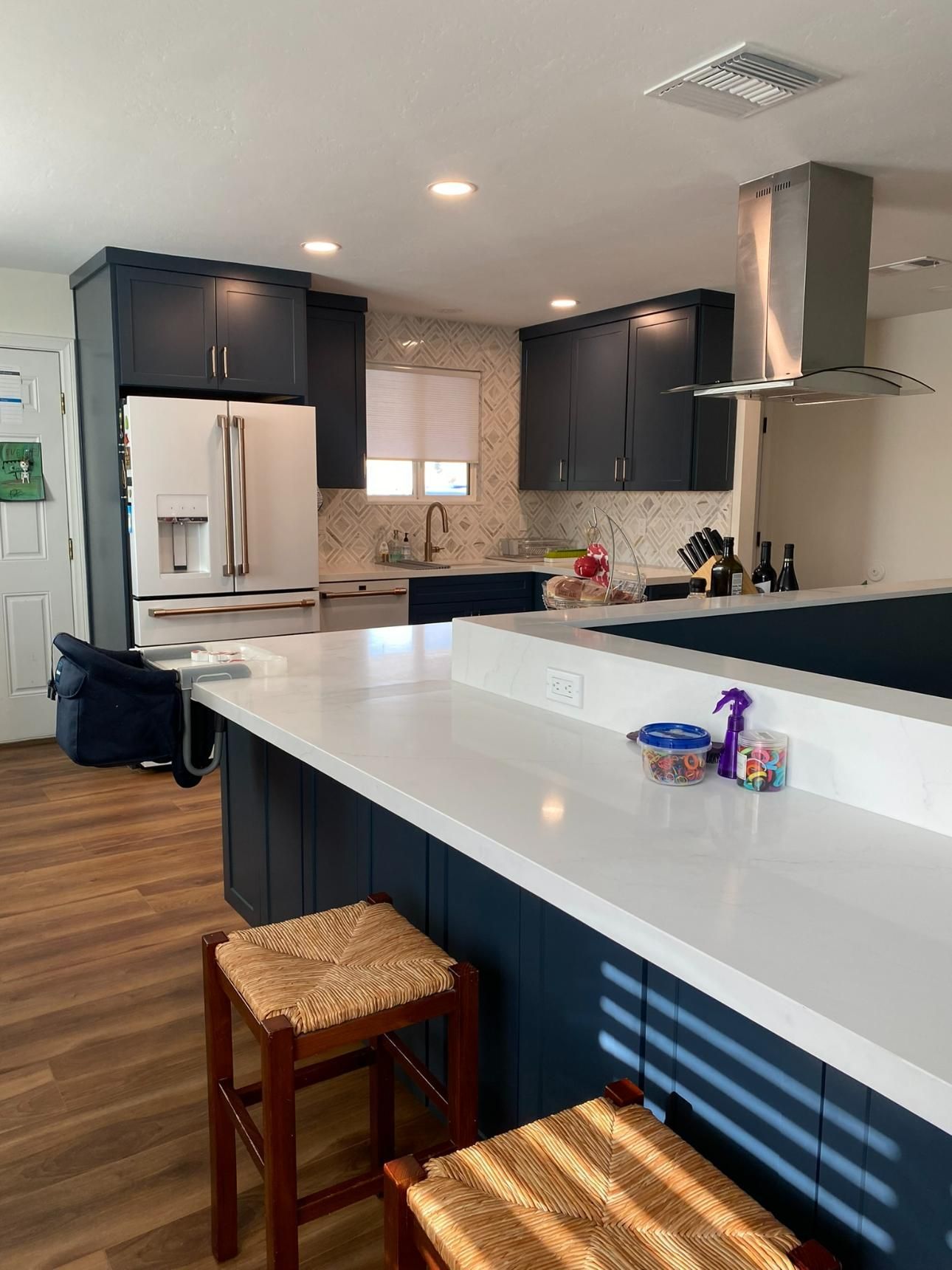 Modern kitchen with white island, dark cabinets, stainless fridge, and two wooden stools