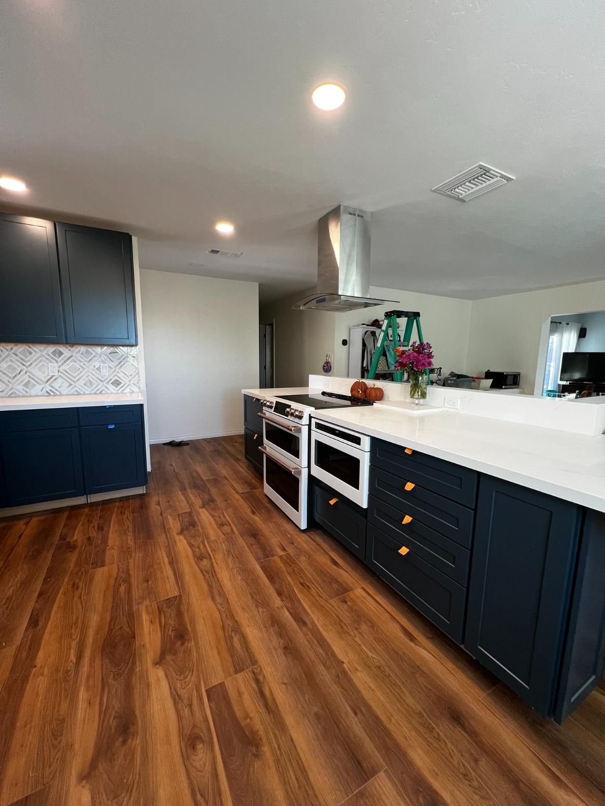 Modern kitchen with dark cabinets, white island, wood floors, and stainless steel range hood