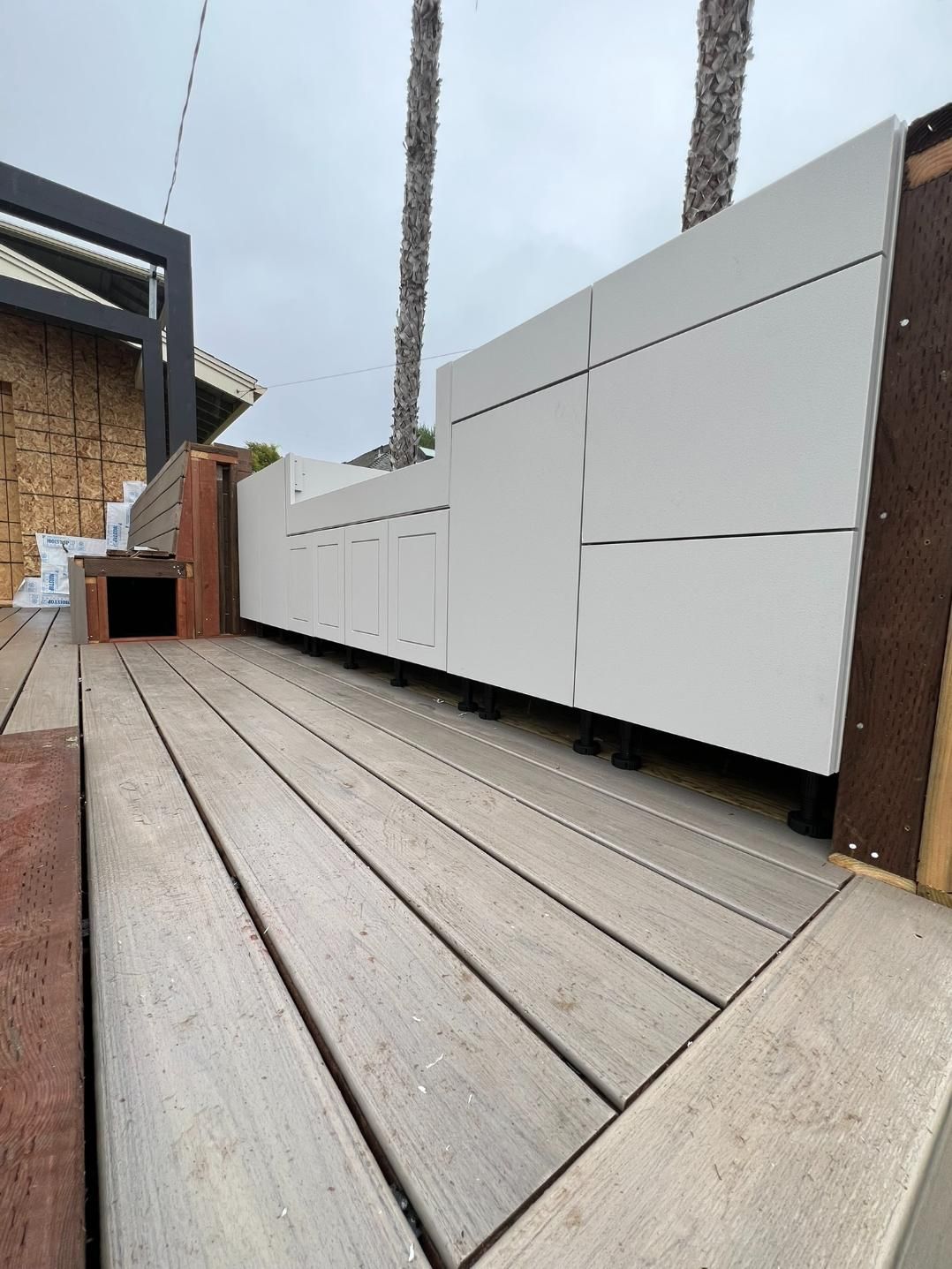 Wooden deck with white outdoor storage cabinets along a wall, viewed from a low angle