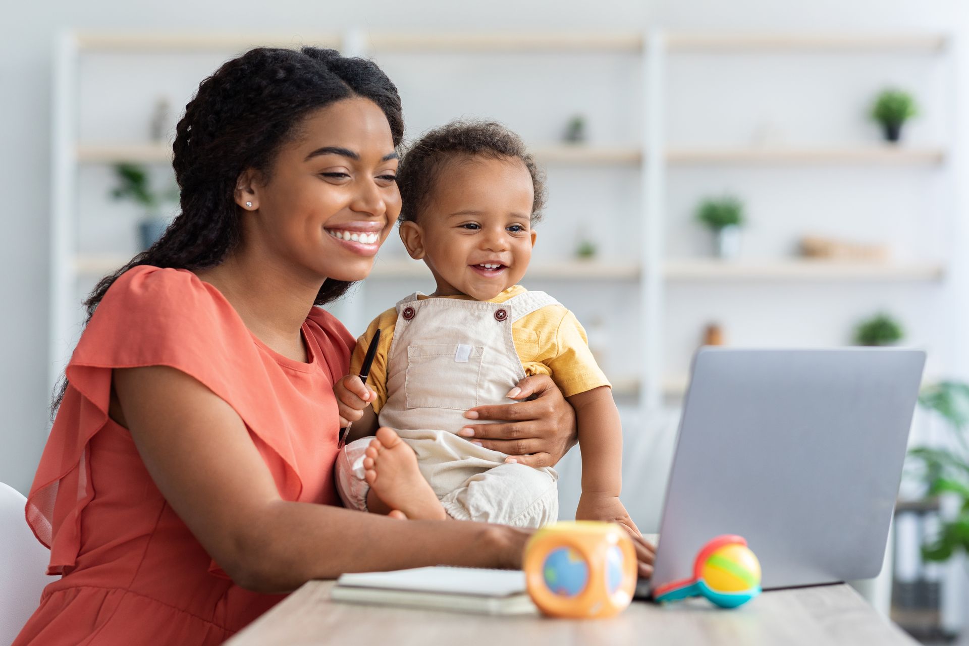 A woman is holding a baby while using a laptop computer.