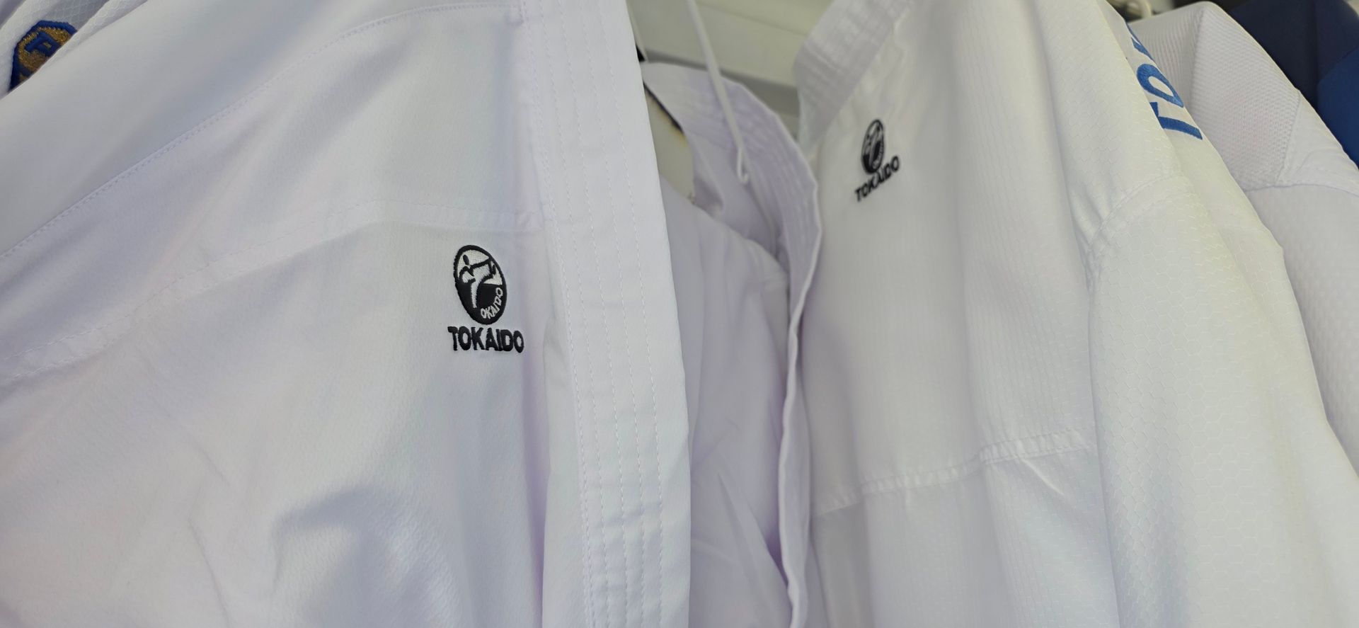 White martial arts uniforms hanging side by side, with black logo patches on the chest