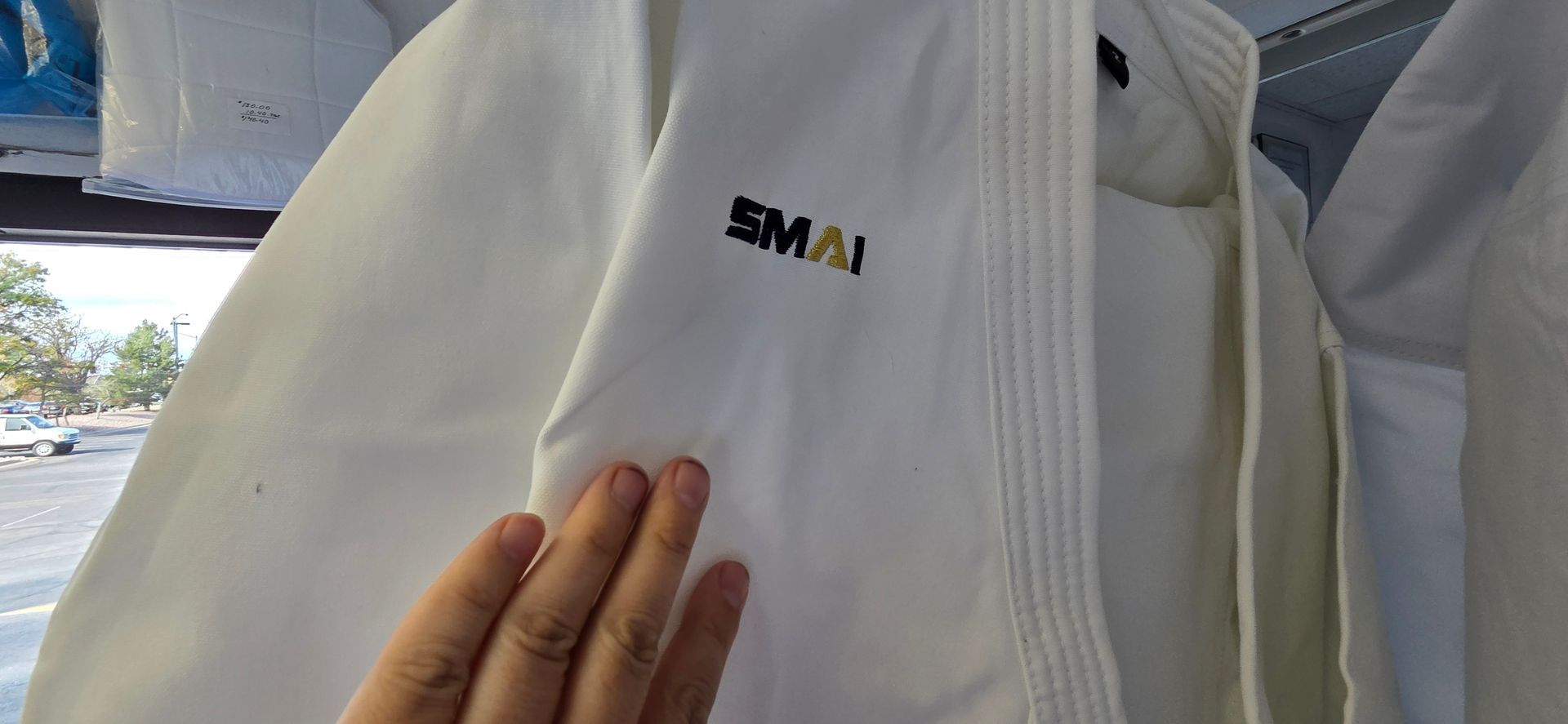 Hand touching a white shirt with a small black-and-green logo hanging indoors